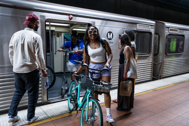 Two women of color existing a subway car with their bikes while two other people wait to enter the car.